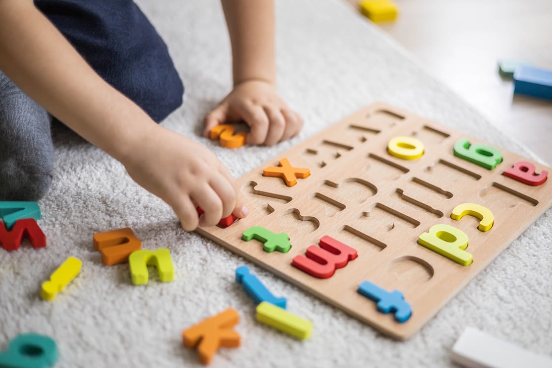 Male kid playing with wooden eco friendly alphabet letters board on table top view intellectual game